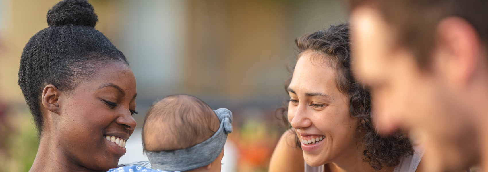 People of different races sharing a meal, smiling at baby